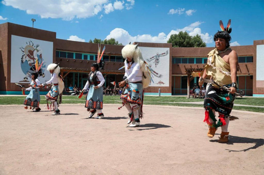 Native American dancers in a row dancing outside of the Indian Cultural center